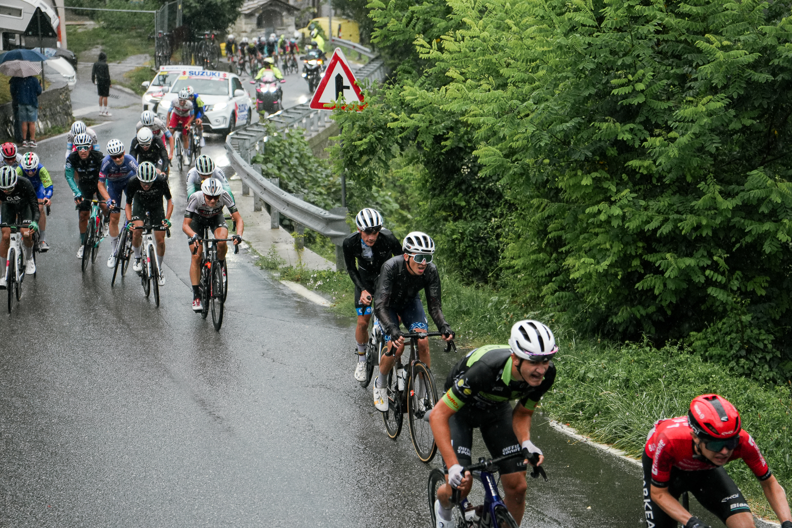 Ciclista en carrera de ruta bajo la lluvia siguiendo al coche del equipo